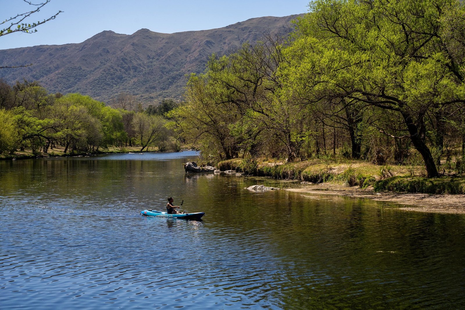 persona haciendo kayak en el rio cosquin con las montañas de fondo